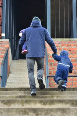 Baba, küçük kızının elini tutuyor ve sonbaharda merdivenleri çıkarken oğullarının elini tutuyor. Baba ve çocuklar birlikte vakit geçiriyorlar..