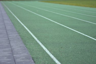 Beyaz çizgileri olan yeşil koşu pisti. Sol tarafta patika, sağ tarafta yeşil çim..