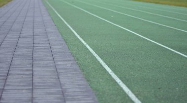 Beyaz çizgileri olan yeşil koşu pisti. Sol tarafta patika, sağ tarafta yeşil çim..