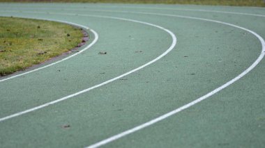 Beyaz çizgiler ve kenarlarında yeşil çimenler olan yeşil koşu yolu eğrisi.