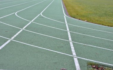 Yeşil koşu yolu beyaz çizgiler ve sağ tarafta yeşil çimlerle dönüyor..