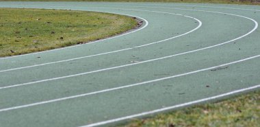 Beyaz çizgiler ve kenarlarında yeşil çimenler olan yeşil koşu yolu eğrisi.