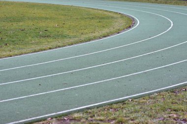 Beyaz çizgiler ve kenarlarında yeşil çimenler olan yeşil koşu yolu eğrisi.