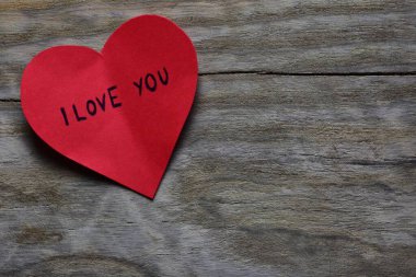 Tahta döşemeli arka planda, sevgililer günü için kırmızı kalp şeklindeki kağıtta seni seviyorum mesajı. Sevgililer günü kartında seni seviyorum yazıyor. Minimalist Sevgililer Günü.