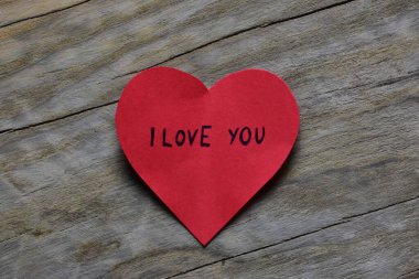 Tahta döşemeli arka planda, sevgililer günü için kırmızı kalp şeklindeki kağıtta seni seviyorum mesajı. Sevgililer günü kartında seni seviyorum yazıyor. Minimalist Sevgililer Günü.