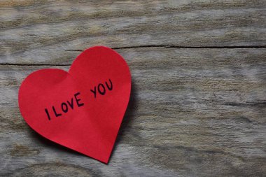 Tahta döşemeli arka planda, sevgililer günü için kırmızı kalp şeklindeki kağıtta seni seviyorum mesajı. Sevgililer günü kartında seni seviyorum yazıyor. Minimalist Sevgililer Günü.