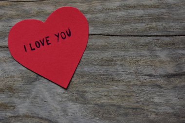Tahta döşemeli arka planda, sevgililer günü için kırmızı kalp şeklindeki kağıtta seni seviyorum mesajı. Sevgililer günü kartında seni seviyorum yazıyor. Minimalist Sevgililer Günü.