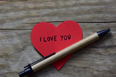 Sevgililer günü için kırmızı kalp şeklindeki kağıtta, tahta bir arka planda, geri dönüşümlü kağıttan yapılmış sürdürülebilir kalemin yanında seni seviyorum mesajı. Sevgililer günü kartında 