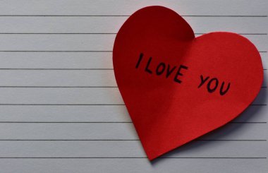 Not defteri arkaplanındaki sevgililer günü için kırmızı kalp şeklindeki kağıtta seni seviyorum mesajı. Sevgililer günü kartında seni seviyorum yazıyor. Minimalist Sevgililer Günü.