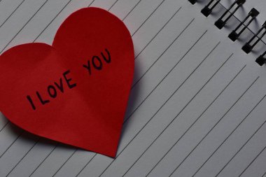 Sevgililer günü için kırmızı kalp şeklindeki kağıtta açık sayfa arkaplanındaki sarmal defter mesajında seni seviyorum. Sevgililer günü kartında seni seviyorum yazıyor. Minimalist Sevgililer Günü.