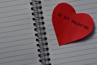 Mesaj metni, sevgililer günü için kırmızı kalp şeklindeki kağıt kart üzerinde açık sayfa arkaplanlı, sarmal defter şeklinde. Sevgililer günü kartında sözcükler benim sevgilim olsun. Minimalist Sevgililer Günü.