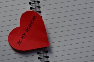 Mesaj metni, sevgililer günü için kırmızı kalp şeklindeki kağıt kart üzerinde açık sayfa arkaplanlı, sarmal defter şeklinde. Sevgililer günü kartında sözcükler benim sevgilim olsun. Minimalist Sevgililer Günü.