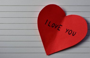 Not defteri arkaplanındaki sevgililer günü için kırmızı kalp şeklindeki kağıtta seni seviyorum mesajı. Sevgililer günü kartında seni seviyorum yazıyor. Minimalist Sevgililer Günü.