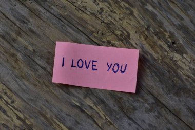 Tahta döşemeli arka planda sevgililer günü için pembe yapışkan notta seni sevdiğimi söyle.