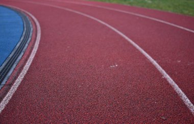 Sol tarafta mavi spor sahası ve sağ tarafta yeşil çimenler olan kırmızı koşu eğrisi.