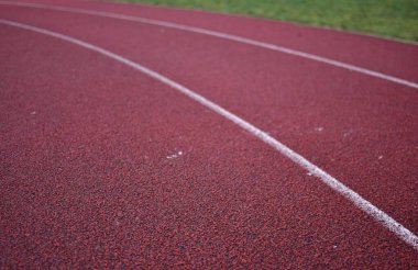 Sağ tarafında yeşil çimen olan kırmızı koşu yolu eğrisi.