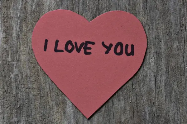 Tahta döşemeli arka planda, sevgililer günü için kırmızı kalp şeklindeki kağıtta seni seviyorum mesajı. Sevgililer günü kartında seni seviyorum yazıyor. Minimalist Sevgililer Günü.