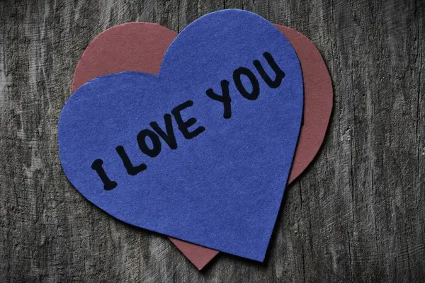 Seni mavi kalp şeklindeki kağıt kartta seviyorum. Tahta ahşap kaplamalı arkaplanda sevgililer günü için. Sevgililer günü kartında seni seviyorum yazıyor. Minimalist Sevgililer Günü.