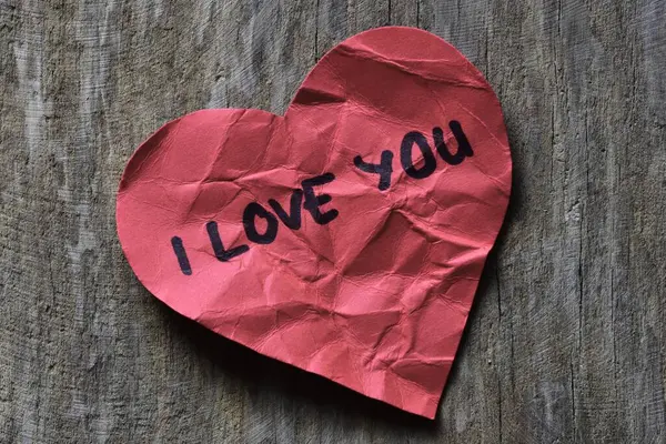 Tahta desenli arka planda, sevgililer günü için buruşuk kırmızı kalp şeklinde kağıt üzerinde seni seviyorum mesajı. Kırık Sevgililer Günü kartında seni seviyorum yazıyor. Reddedilmiş sevgililer günü tebrikleri..