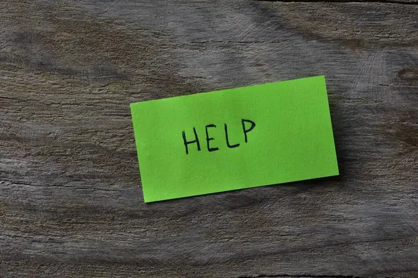 Tahta döşemeli arka plandaki yeşil yapışkan nota mesaj yardımı. Not kağıdına kelime yardımı yazan bir kalem.