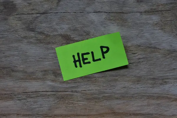 Tahta döşemeli arka plandaki yeşil yapışkan nota mesaj yardımı. Siyah kalem not kağıdına kelime yardımı yazdı.