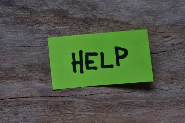 Tahta döşemeli arka plandaki yeşil yapışkan nota mesaj yardımı. Siyah kalem not kağıdına kelime yardımı yazdı.