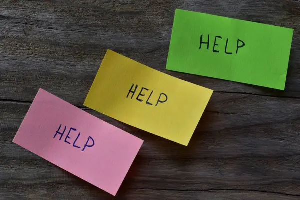 Tahta kaplamalı arka planda pembe yeşil ve sarı yapışkan notlar için mesaj yardımı. Not kağıdına kelime yardımı yazan bir kalem.