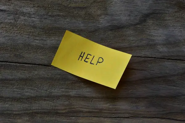 Tahta döşemeli arka plandaki sarı yapışkan nota mesaj yardımı. Not kağıdına kelime yardımı yazan bir kalem.