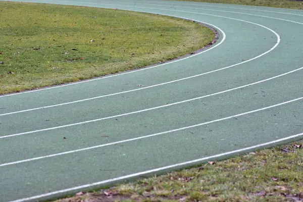 Beyaz çizgiler ve kenarlarında yeşil çimenler olan yeşil koşu yolu eğrisi.