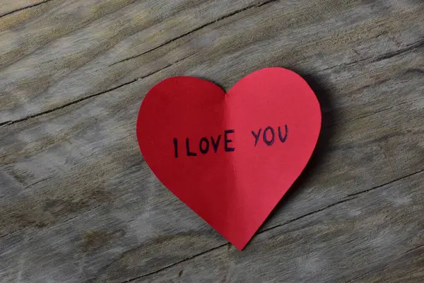 Tahta döşemeli arka planda, sevgililer günü için kırmızı kalp şeklindeki kağıtta seni seviyorum mesajı. Sevgililer günü kartında seni seviyorum yazıyor. Minimalist Sevgililer Günü.