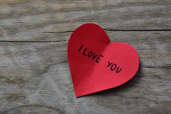 Tahta döşemeli arka planda, sevgililer günü için kırmızı kalp şeklindeki kağıtta seni seviyorum mesajı. Sevgililer günü kartında seni seviyorum yazıyor. Minimalist Sevgililer Günü.
