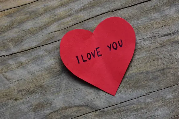 Tahta döşemeli arka planda, sevgililer günü için kırmızı kalp şeklindeki kağıtta seni seviyorum mesajı. Sevgililer günü kartında seni seviyorum yazıyor. Minimalist Sevgililer Günü.