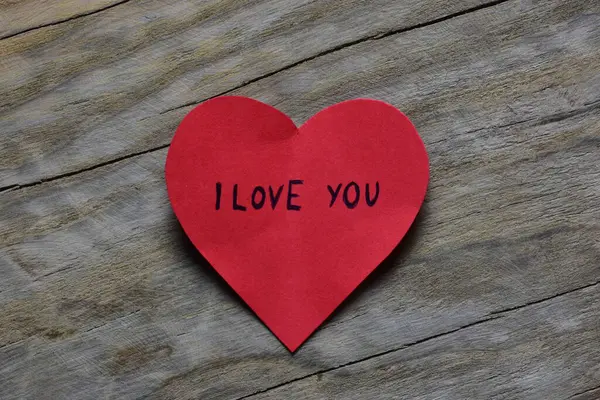 Tahta döşemeli arka planda, sevgililer günü için kırmızı kalp şeklindeki kağıtta seni seviyorum mesajı. Sevgililer günü kartında seni seviyorum yazıyor. Minimalist Sevgililer Günü.