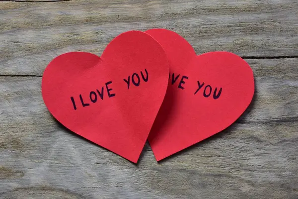 Tahta döşemeli arka planda, sevgililer günü için kırmızı kalp şeklindeki kağıtta seni seviyorum mesajı. İçinde seni seviyorum yazan iki Sevgililer Günü kartı. Minimalist Sevgililer Günü.