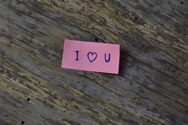 Tahta döşemeli arka planda sevgililer günü için pembe yapışkan notta seni sevdiğimi söyle.