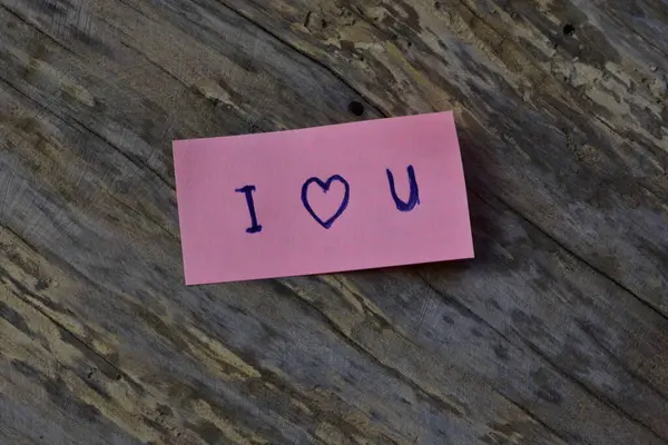 Tahta döşemeli arka planda sevgililer günü için pembe yapışkan notta seni sevdiğimi söyle.
