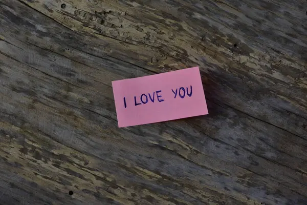 Tahta döşemeli arka planda sevgililer günü için pembe yapışkan notta seni sevdiğimi söyle.