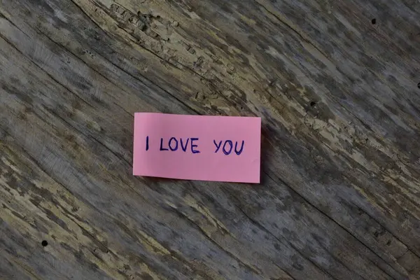 Tahta döşemeli arka planda sevgililer günü için pembe yapışkan notta seni sevdiğimi söyle.