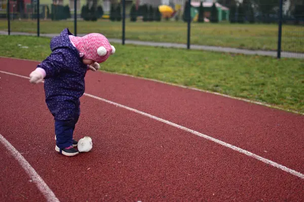 Yavru kız, soğuk sonbaharda okul stadyumunda buz parçası keşfediyor. Küçük kız kışın eğleniyor..