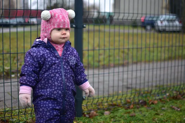 Soğuk sonbaharda metal tel örgülerin yanında dikilen ve gülümseyen küçük kız. Küçük kız kışın eğleniyor..