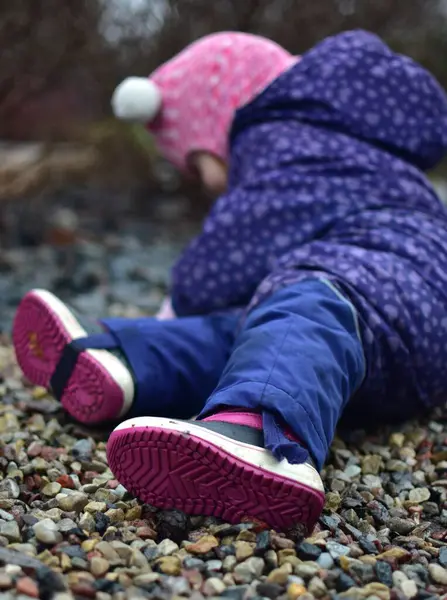 Yavru kız soğuk sonbaharda parkta küçük kayaların üzerinde oturuyor. Küçük kız kışın eğleniyor..