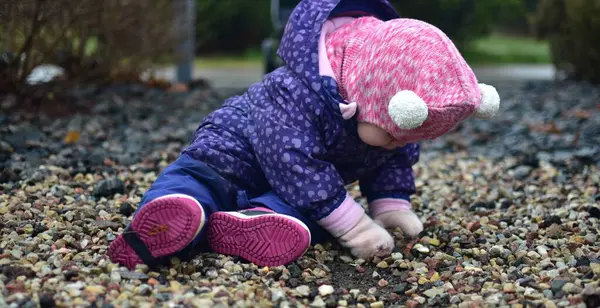 Yavru kız soğuk sonbaharda parkta küçük kayalarla oturuyor ve oynuyor. Küçük kız kışın eğleniyor..