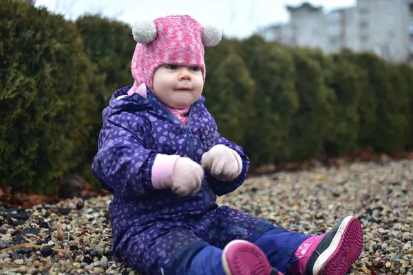 Yavru kız soğuk sonbaharda parkta küçük kayaların üzerinde oturuyor. Küçük kız kışın eğleniyor..