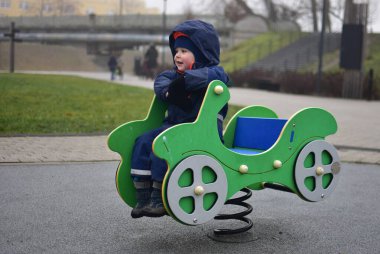 Küçük çocuk yeşil arabada oturuyor. Çocuk parkında sallanıyor ve sonbaharda gülümsüyor.
