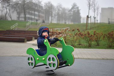 Küçük çocuk yeşil arabada oturuyor. Çocuk parkında sallanıyor ve sonbaharda gülümsüyor.