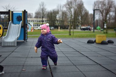 Soğuk sonbaharda, şehir parkındaki çocuk parkında oynayan bir kız bebek. Küçük kız kışın halk parkında eğleniyor.