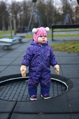 Küçük kız, soğuk kış zamanı halk parkında trambolinde oynuyor. Bebeğim sonbaharda trambolinde eğleniyor.