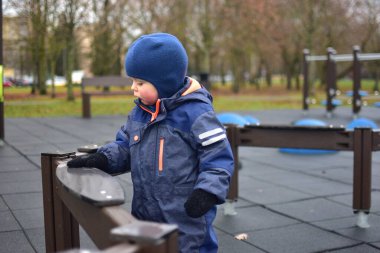 Düşünceli küçük çocuk parktaki parklarda parlayan kollarıyla oyun aletlerine dokunuyor. Kışın soğuk havada dışarıda oynayan bir çocuk..