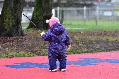 Yavru kız, soğuk kış mevsiminde elinde ağaç dalları, elinde çocuk parkında duruyor.