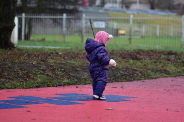 Yavru kız, soğuk kış mevsiminde elinde ağaç dalları, elinde çocuk parkında duruyor.